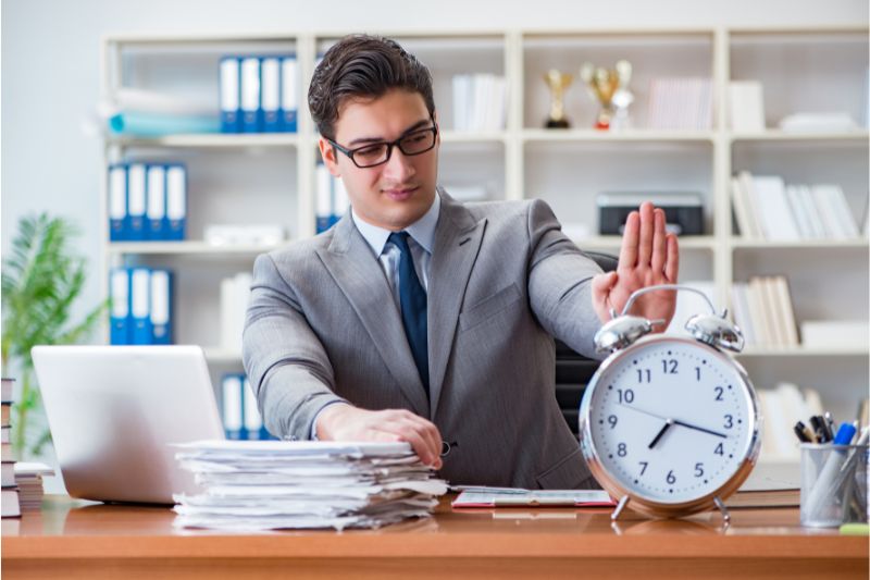 man pushing alarm clock on wooden table