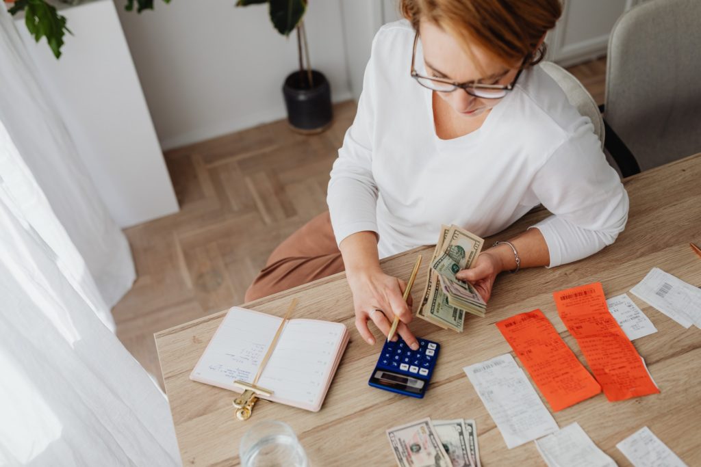 Woman using a calculator with receipts and cash in front of her.