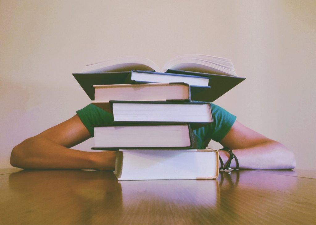 An accounting student hidden behind a large pile of thick books