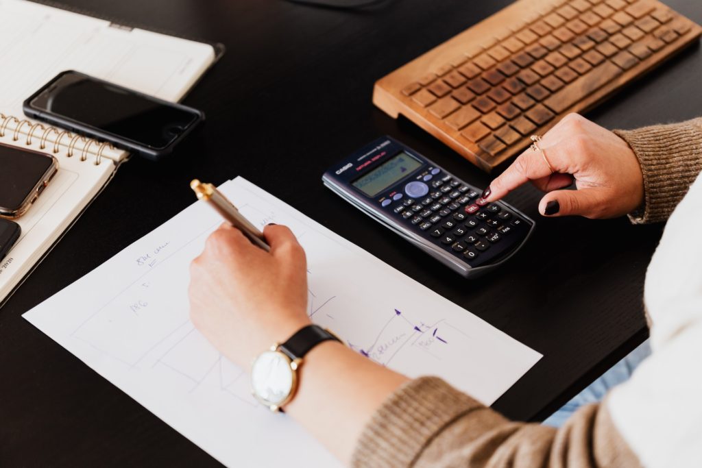 A lady writing on a A4 piece of paper while doing calculations