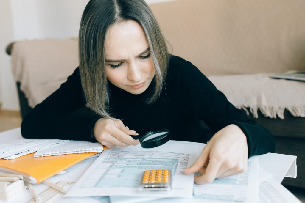 A woman carefully analyzing spreadsheets and bank accounts using a magnifying glass