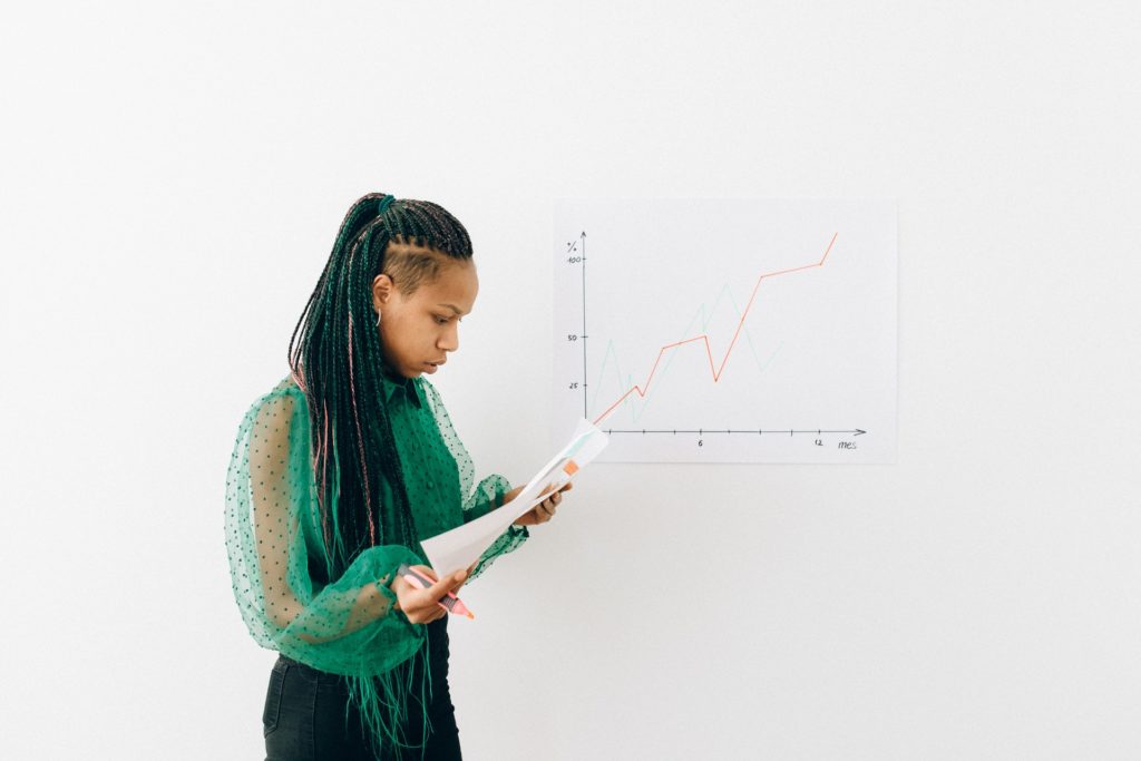 Woman in green blouse studying a sheet of paper while standing in front of a white board