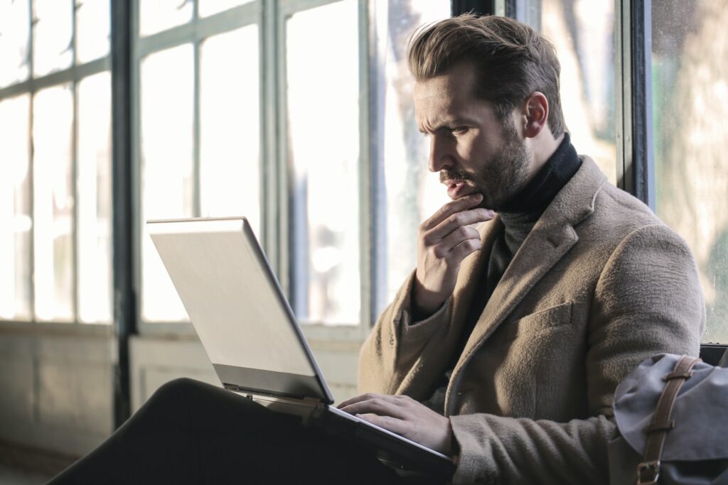 A man in a brown suit and a grey laptop, thinking about which accounting exam he should take