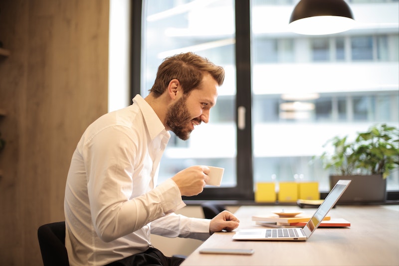 man in front of a laptop holding cup