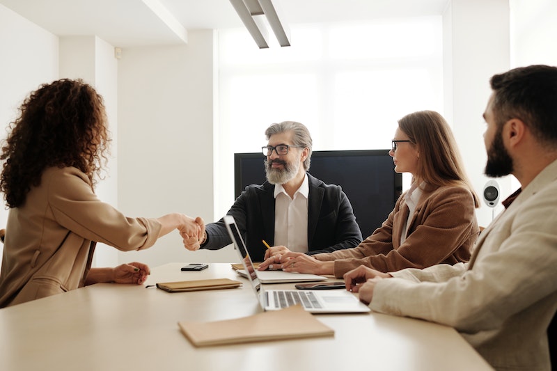 man in a black suit shaking hands of a woman in brown long sleeve in the office