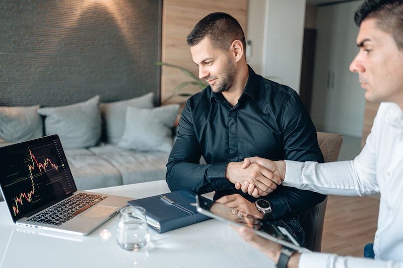 Two Men Shaking Hands While Looking at a Laptop 