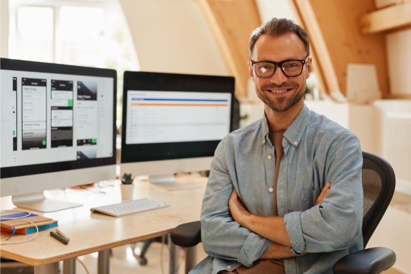 man smiling at work behind two computer screens