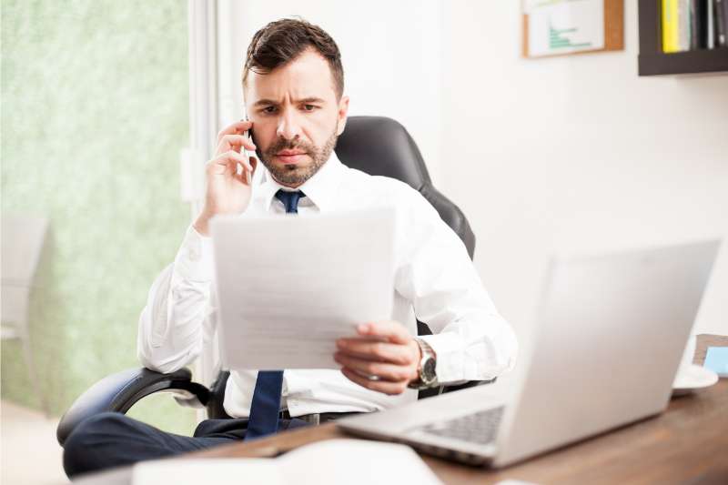 man making a phone call while looking at paper