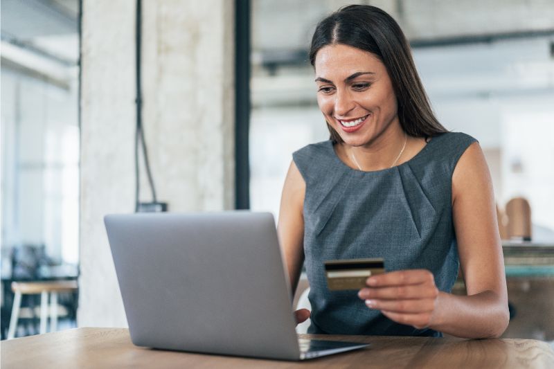 woman smiling while holding a credit card in front of a laptop